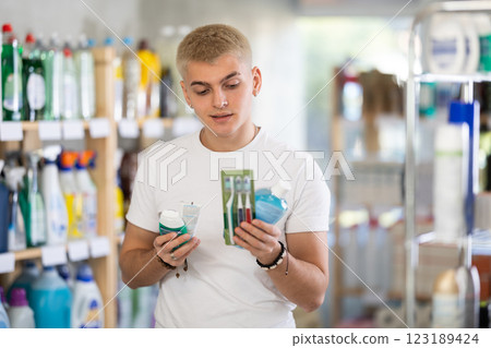Positive young man choosing toothpaste and toothbrush, dental kit in store 123189424