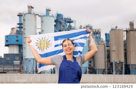Cheerful young woman in workwear holds the national flag of Uruguay 123189429