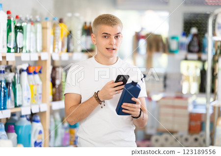 Positive young guy buyer in shop holding and choosing spray, scan QR code 123189556
