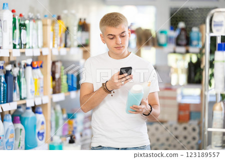 Positive young man buyer in shop holding and choosing shampoo or shower gel, scan QR code on label Positive young man buyer in shop holding and choosing shampoo or shower gel, scan QR code on label 123189557