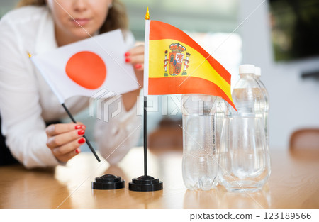 Young woman putting flags of Japan and Spain on table in office 123189566