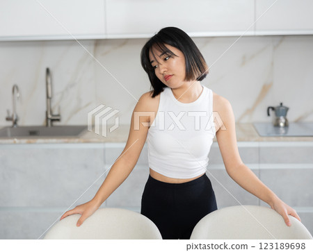 Sad young Asian girl standing at table in the kitchen Sad young Asian girl standing at table in the kitchen 123189698