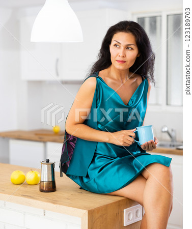 Portrait of woman sitting on table in kitchen and drinking coffee Portrait of woman sitting on table in kitchen and drinking coffee 123189703