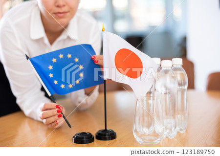 Female hands placing flag of European Union and Japan on table before negotiations 123189750