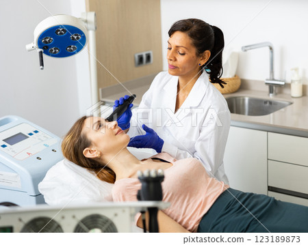 Hispanic woman beautician doing needle-free mesotherapy for young woman Hispanic woman beautician doing needle-free mesotherapy for young woman 123189873