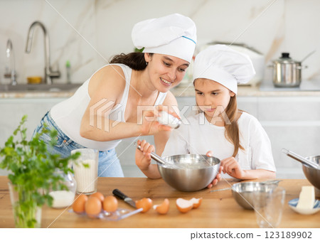 Mom and girl prepare dough for baking, mom adds salt to bowl, girl mixes ingredients with whisk. Mom and girl prepare dough for baking, mom adds salt to bowl, girl mixes ingredients with whisk. 123189902