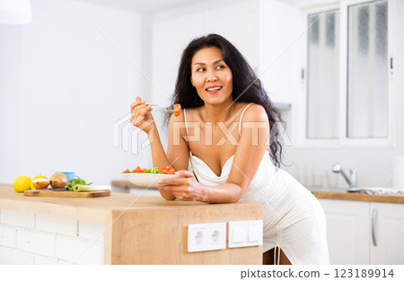 Portrait of positive woman in nightdress eating salad at home 123189914