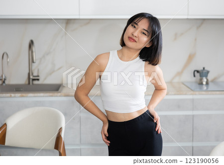 Smiling young Asian girl standing at table in the kitchen 123190056