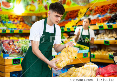 Male shop assistant lays potatoes on counter in grocery shop Male shop assistant lays potatoes on counter in grocery shop 123190148