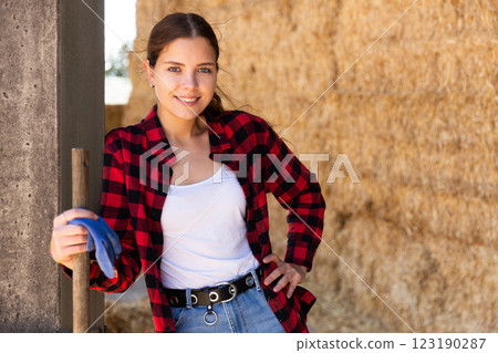 Portrait of a young positive farmer girl standing near haystacks Portrait of a young positive farmer girl standing near haystacks 123190287