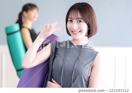 年輕女子微笑著,手拿瑜珈墊,做出 V 形手勢 年輕女子微笑著,手拿瑜珈墊,做出 V 形手勢 123191512