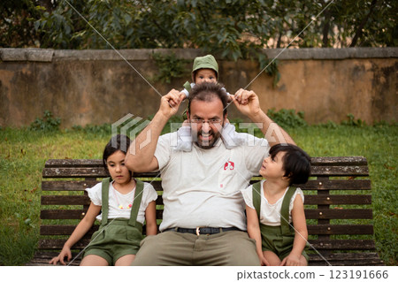 dad sitting with small baby and two elder children on the bench in the park dad sitting with small baby and two elder children on the bench in the park 123191666