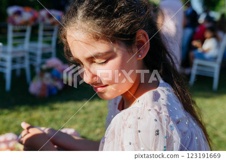 A girl in a pink dress is sitting with eyes closed under bright sun 123191669