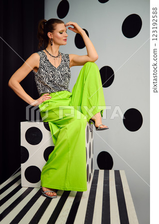 Graceful woman sits in bold green outfit against playful polka dot backdrop Graceful woman sits in bold green outfit against playful polka dot backdrop 123192588