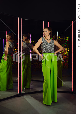 Model showcasing vibrant green pants and stylish top in a modern reflective setting Model showcasing vibrant green pants and stylish top in a modern reflective setting 123192594