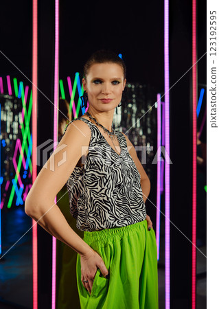 Elegant model poses confidently in neon-lit studio with vibrant background and striking outfit 123192595