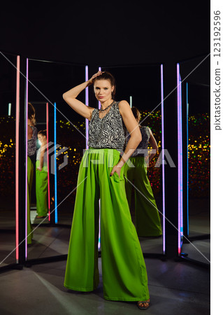 Model showcases vibrant green pants and patterned top in a stylish indoor setting with mirrors 123192596