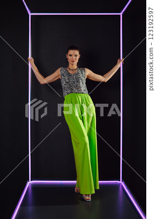 Stylish model showcases contemporary fashion in vibrant green outfit against dark backdrop Stylish model showcases contemporary fashion in vibrant green outfit against dark backdrop 123192597