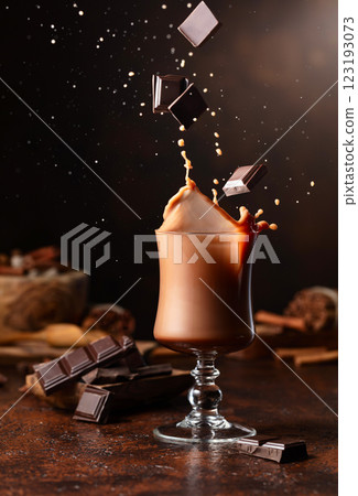 Pieces of dark chocolate fall into a glass of cocoa drink. 123193073