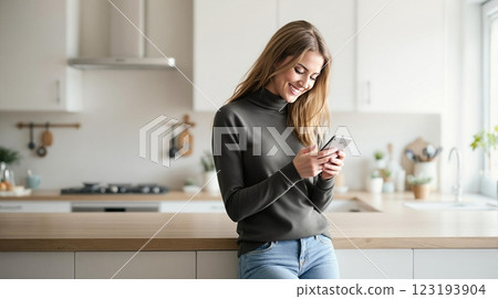 Smiling Woman Using Smartphone in Contemporary White Kitchen Interior 123193904