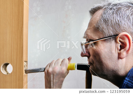 Chiseling groove in door leaf for latch installation, mortising cutting recess into wood to accommodate latch, using chisel to remove material. Chiseling groove in door leaf for latch installation, mortising cutting recess into wood to accommodate latch, using chisel to remove material. 123195059