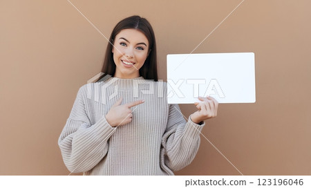 Cheerful Young Woman in Knitted Sweater Pointing at Blank Card Against Solid Background - Mockup Template for Advertisement or Announcement 123196046