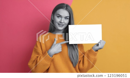 Cheerful Young Woman in Knitted Sweater Pointing at Blank Card Against Solid Background - Mockup Template for Advertisement or Announcement 123196051