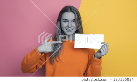 Cheerful Young Woman in Knitted Sweater Pointing at Blank Card Against Solid Background - Mockup Template for Advertisement or Announcement 123196054