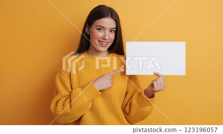Cheerful Young Woman in Knitted Sweater Pointing at Blank Card Against Solid Background - Mockup Template for Advertisement or Announcement 123196057