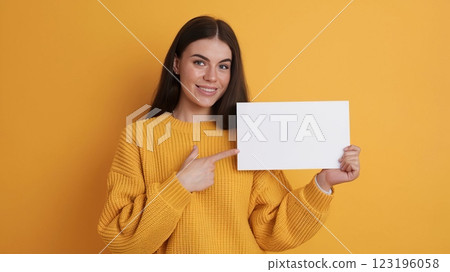Cheerful Young Woman in Knitted Sweater Pointing at Blank Card Against Solid Background - Mockup Template for Advertisement or Announcement 123196058