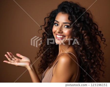 Joyful Woman with Wild  Hair Presenting Empty Space on Palm Against Brown Studio Background, Perfect for Product Placement, Beauty and Hair Care Marketing Mockup Portrait 123196151