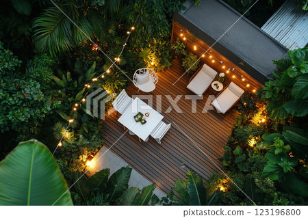 Cozy outdoor seating area with wicker furniture, wooden deck, tropical plants, and string lights top view 123196800