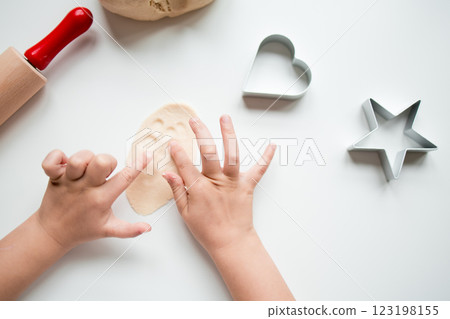 Child hands crafting with dough and cookie cutters in kitchen setting Child hands crafting with dough and cookie cutters in kitchen setting 123198155