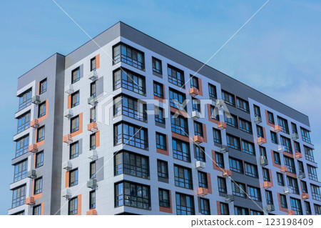 The concept of modern architecture, a residential complex, an apartment building for living. Close-up view from the corner of a multi-storey, apartment building in gray and white tones with orange 123198409