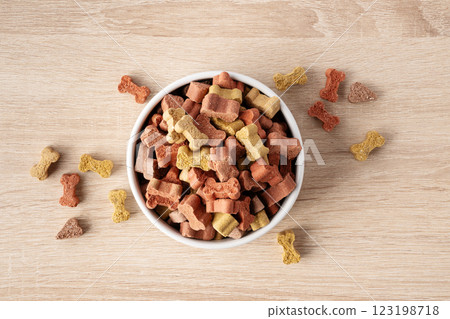 Dry dog food in a shape of bones in bowl on wooden floor background top view. Plate full of mineral healthy dog food. Pet snack in white bowl on floor. 123198718