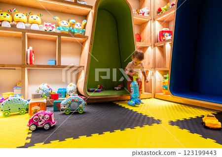 Child playing in colorful playroom with shelves full of toys and a fun interactive vacuum cleaner 123199443