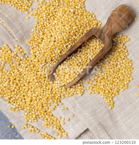 Raw uncooked yellow millet grain in a wooden scoop on grey table, top view. Ancient food 123200110