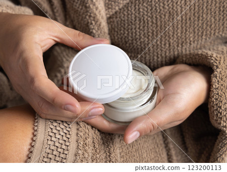 Closeup of woman in brown bathrobe opening white cream jar with hands, cosmetic mockup Closeup of woman in brown bathrobe opening white cream jar with hands, cosmetic mockup 123200113