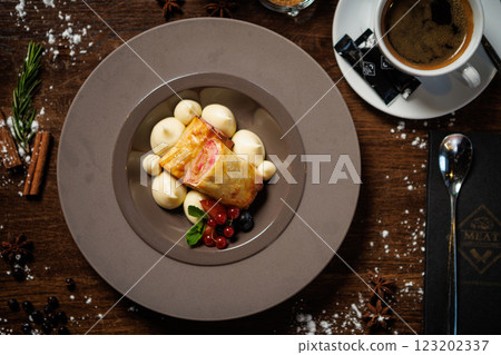 Crispy pastry with berry filling, served with vanilla cream dollops. Decorated with red currants, blueberries, and mint. Sophisticated dessert closeup in modern gourmet restaurant 123202337