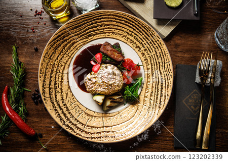 Gold-plated beef steak with grilled vegetables, cherry tomatoes, and a rich sauce. Gourmet dish garnished with edible flowers, served on an elegant plate in a fine dining restaurant Gold-plated beef steak with grilled vegetables, cherry tomatoes, and a rich sauce. Gourmet dish garnished with edible flowers, served on an elegant plate in a fine dining restaurant 123202339