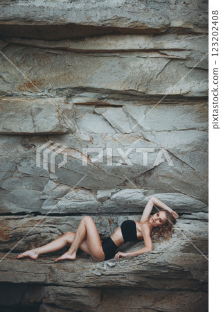Graceful Blonde in Bikini: Reclining Pose on Rocky Shore Graceful Blonde in Bikini: Reclining Pose on Rocky Shore 123202408