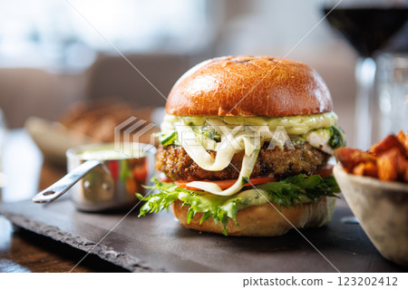 Delicious veggie burger with lettuce, tomato, cheese, and sauce on a toasted bun. Served with a side of sweet potato fries and a small cup of dipping sauce. Perfect for a healthy meal Delicious veggie burger with lettuce, tomato, cheese, and sauce on a toasted bun. Served with a side of sweet potato fries and a small cup of dipping sauce. Perfect for a healthy meal 123202412