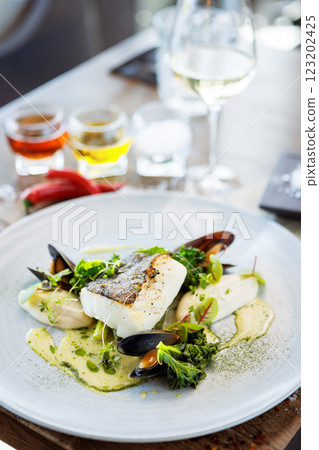 Cod fillet with cauliflower cream, asparagus, clam-wine sauce and mussles. Delicious seafood fish closeup served on a table for lunch in modern cuisine gourmet restaurant Cod fillet with cauliflower cream, asparagus, clam-wine sauce and mussles. Delicious seafood fish closeup served on a table for lunch in modern cuisine gourmet restaurant 123202425