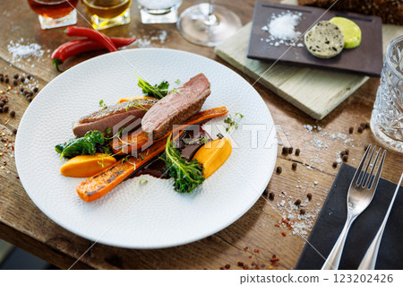 Duck fillet with sweet potato cream, roasted carrots, kale, beet-port sauce on white plate. Grilled and roasted poultry closeup served on a table for lunch in modern cuisine gourmet restaurant. Duck fillet with sweet potato cream, roasted carrots, kale, beet-port sauce on white plate. Grilled and roasted poultry closeup served on a table for lunch in modern cuisine gourmet restaurant. 123202426