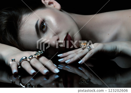 Studio portrait of beautiful and sexy brunette woman with fancy make-up and various rings on her fingers 123202606