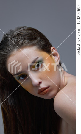Young attractive and confident woman with wet hair and striking green eyeshadow leaning forward against gray studio background. 123202692