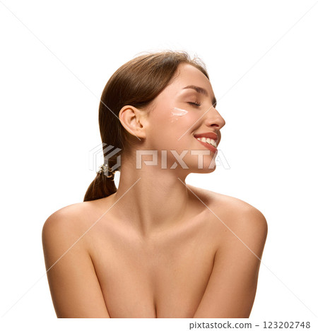 Happy woman, with bare shoulders, smiling with closed eyes, relaxed expression, and skincare cream on cheek against white studio background. Happy woman, with bare shoulders, smiling with closed eyes, relaxed expression, and skincare cream on cheek against white studio background. 123202748
