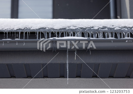 Icicles hanging from a snow-covered eave and black gutter on a modern house during winter, showing frozen water runoff. Icicles hanging from a snow-covered eave and black gutter on a modern house during winter, showing frozen water runoff. 123203753