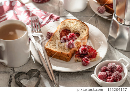 Toasted bread with heart-shaped cut and raspberry jam on tile background in bright morning light. Festive breakfast for Valentines day 123204157