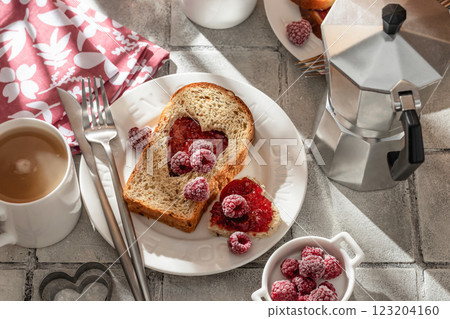 Toasted bread with heart-shaped cut and raspberry jam on tile background in bright morning light, top view. Festive breakfast for Valentines day Toasted bread with heart-shaped cut and raspberry jam on tile background in bright morning light, top view. Festive breakfast for Valentines day 123204160